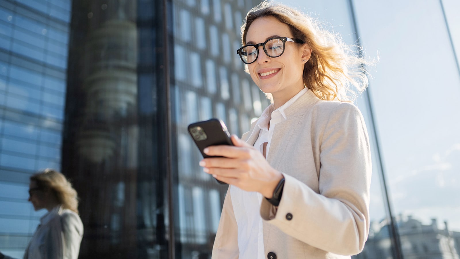 Kvinna i stadsmiljö går och läser på mobiltelefon.